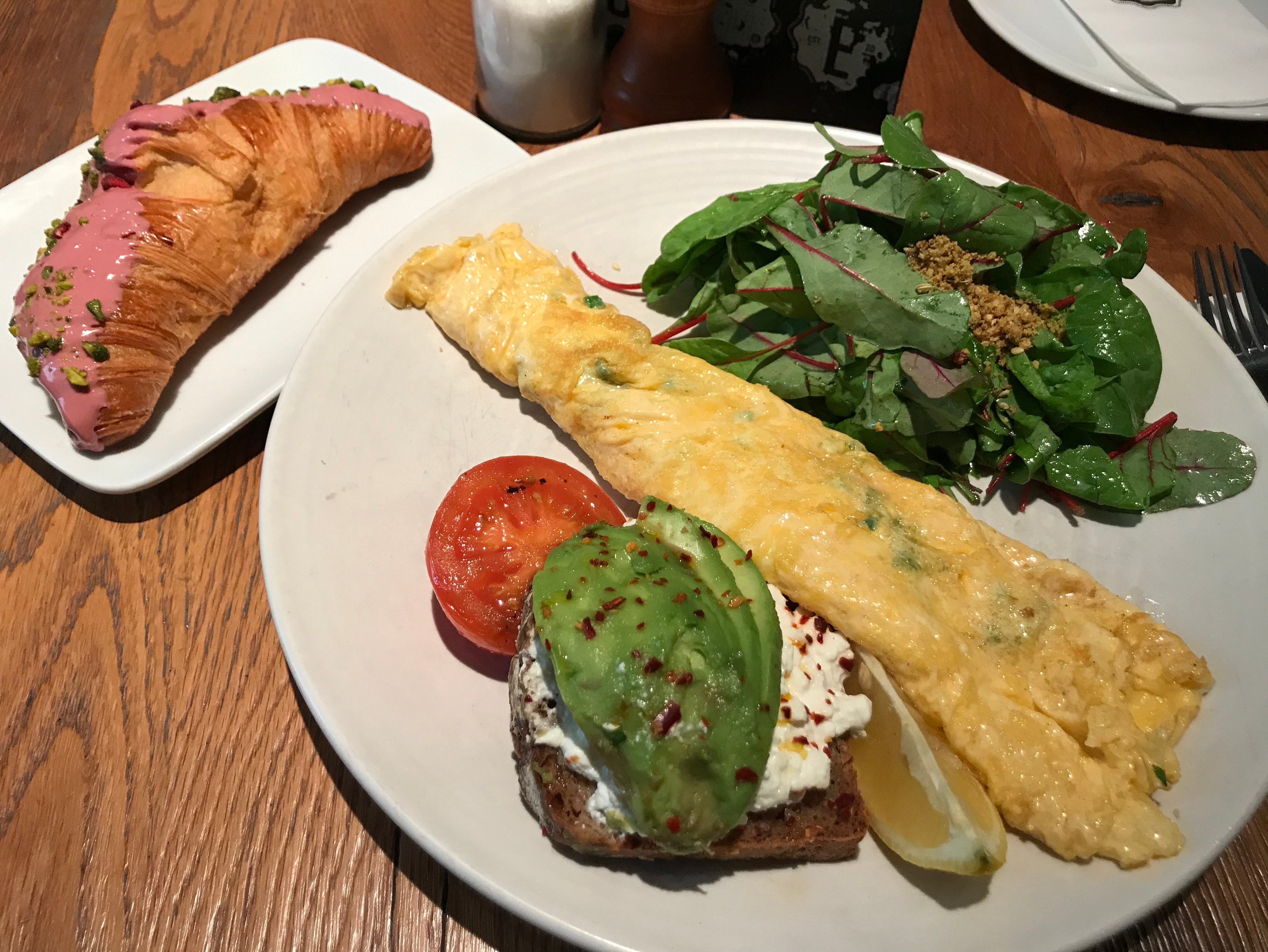 Omelette with avocado toast, salad, and croissant with pink glaze.