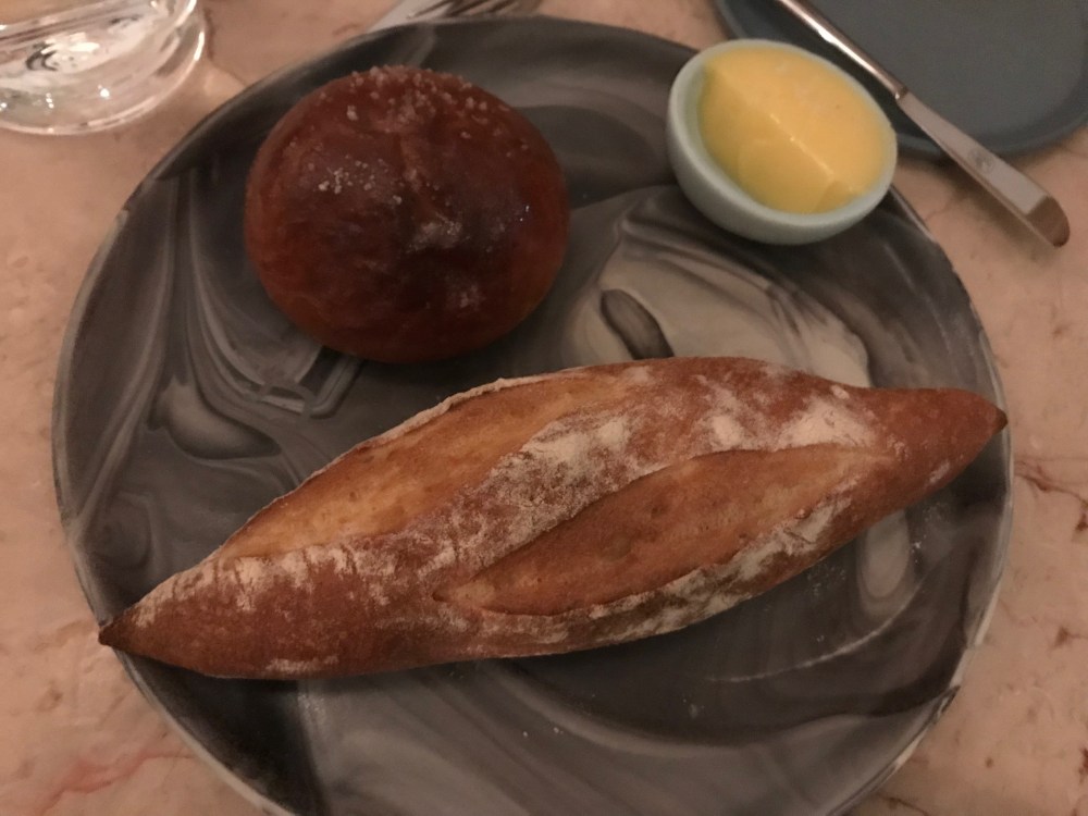 Baguette and milk bun next to butter on marble plate