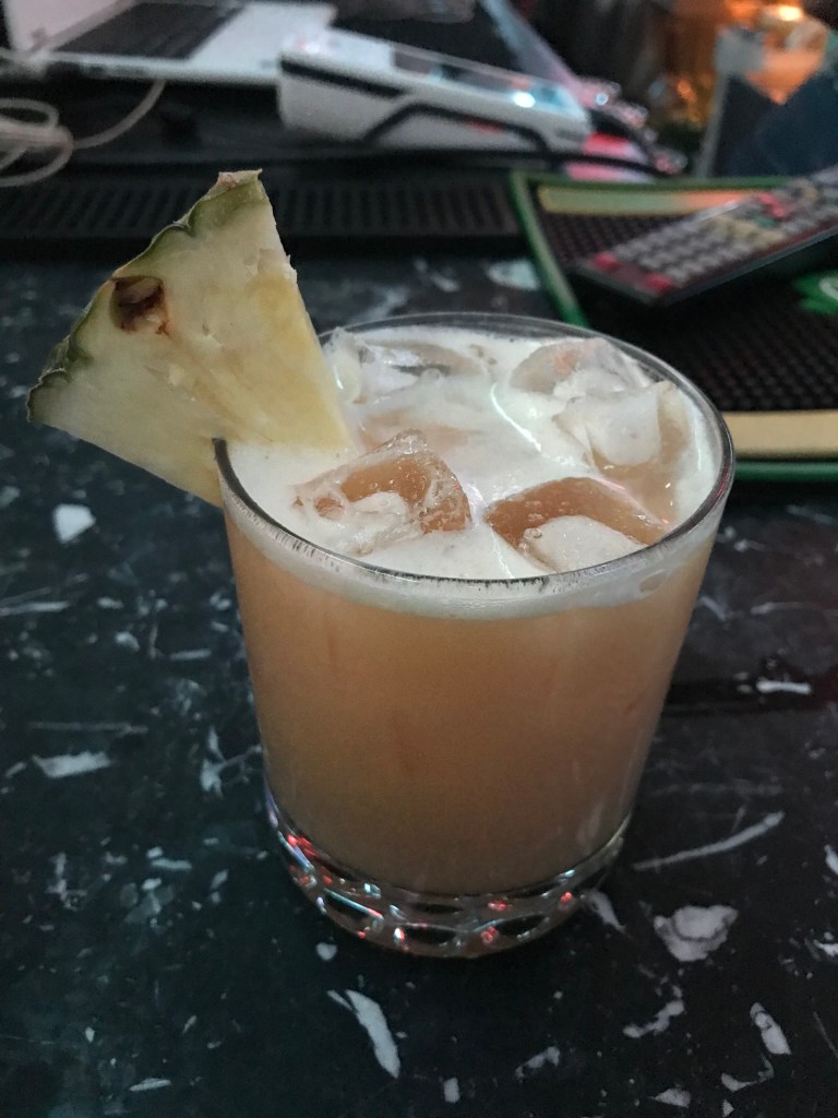 A rum painkiller cocktail in a glass, with a wedge of pineapple on the rim.