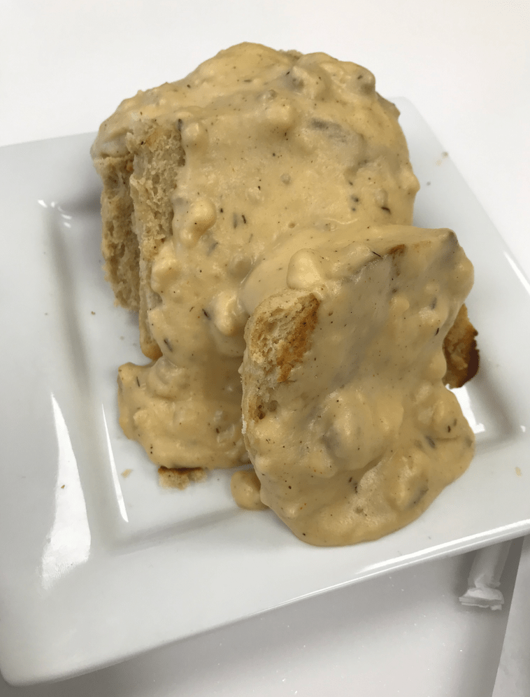 Four biscuits covered in sausage gravy stacked on a white plate.