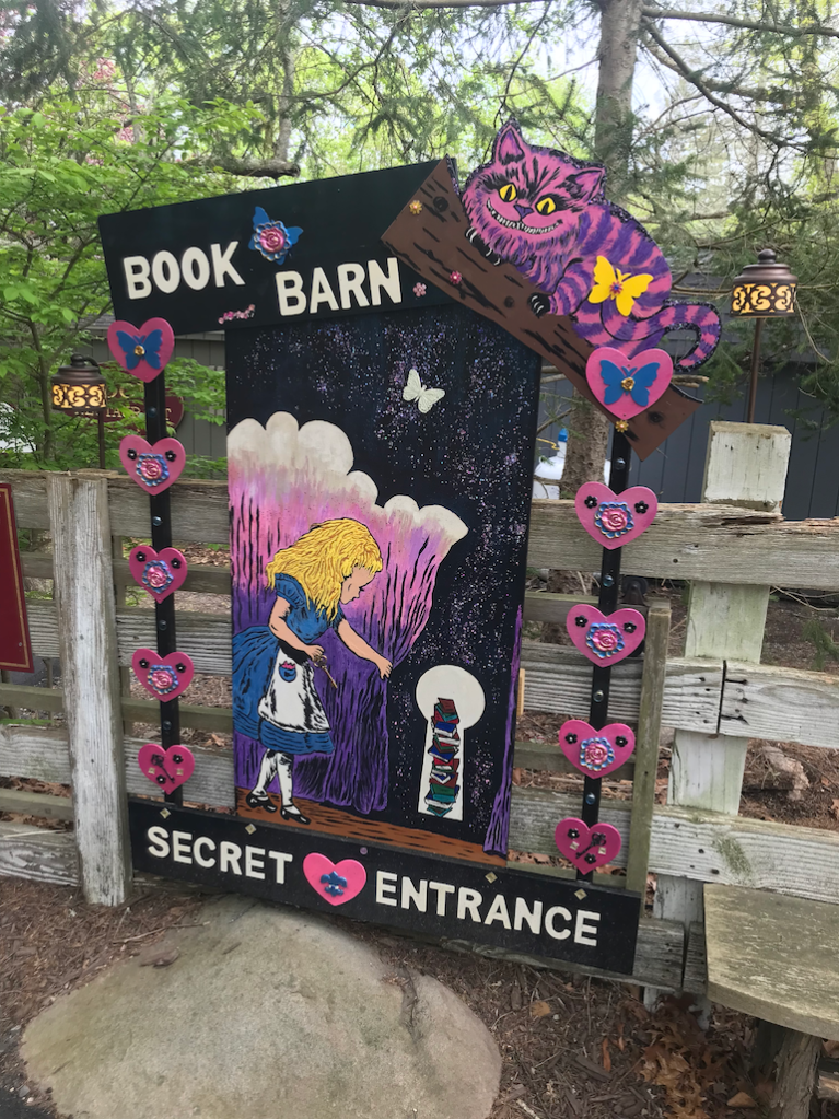 A sign that says Book Barn Secret Entrance decorated with figures from Alice in Wonderland.